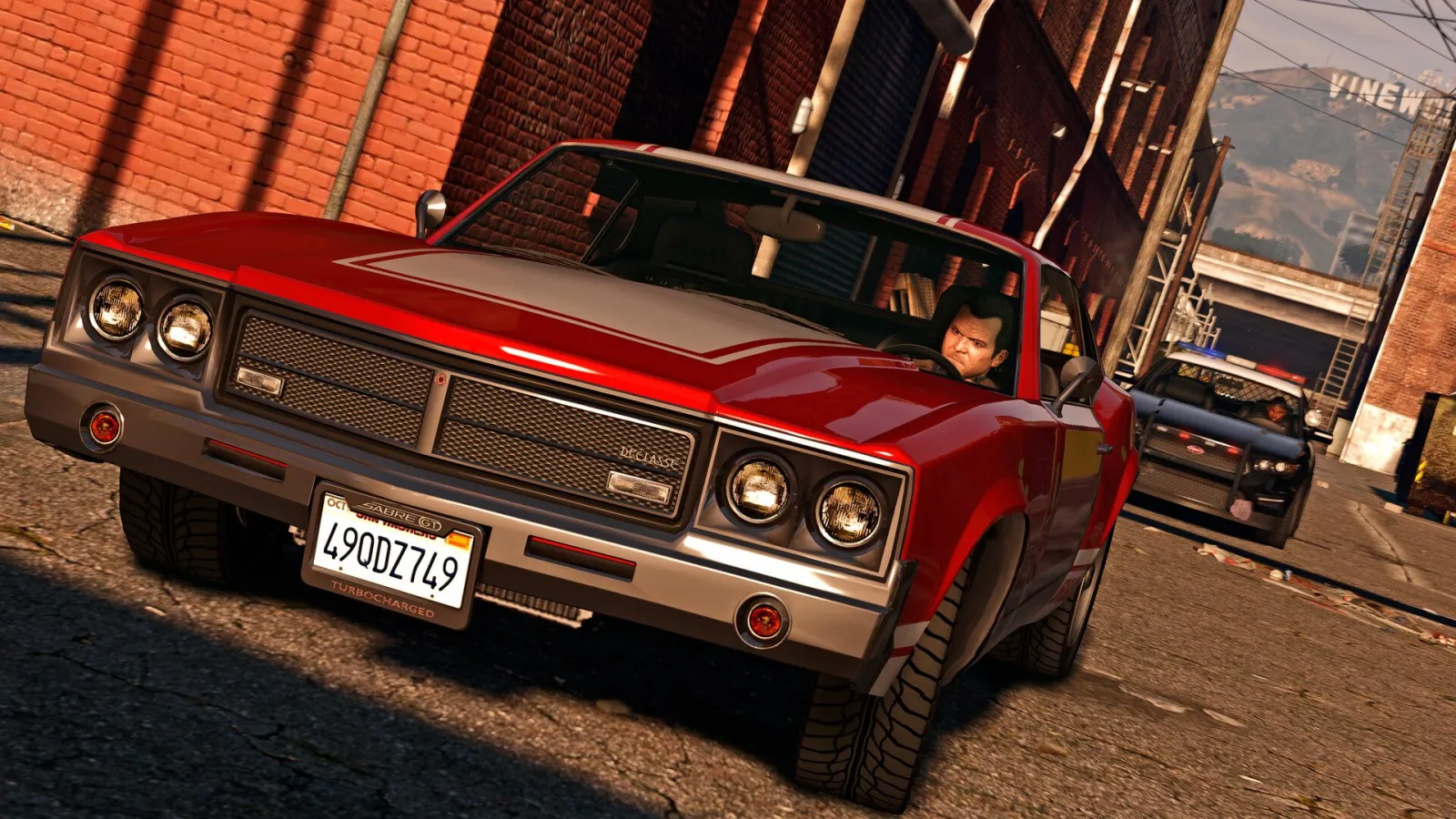 GTA 5’te arkasında polis aracıyla ara sokakta hızlanan kırmızı muscle car
